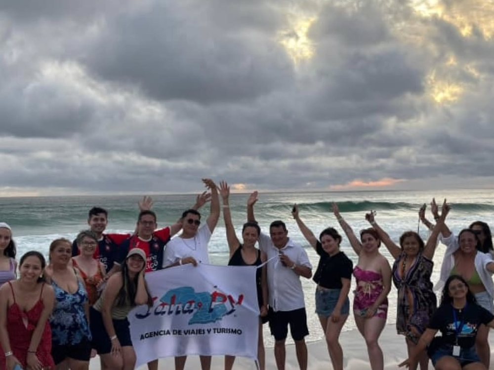 Pasajeros de Jaha PY con la bandera de la agencia en la playa